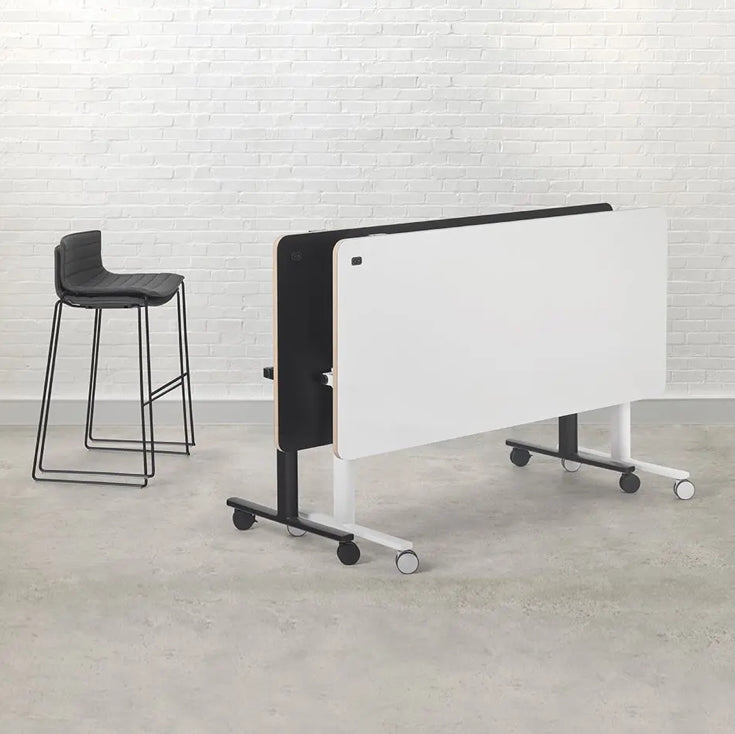 Portable whiteboard on wheels with a black frame against a white brick wall.