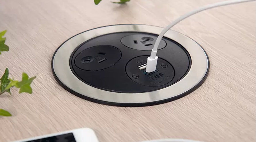 Pop-up electrical outlet with a cable plugged into it on a wooden surface.