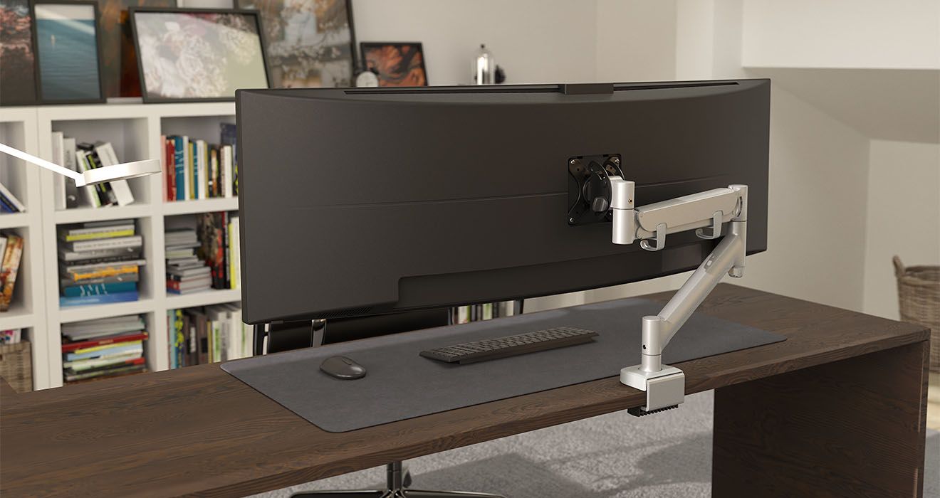 A heavy duty LCD arm mounted on a desk, supporting a widescreen monitor, with a spring-assisted arm and a mounting base.